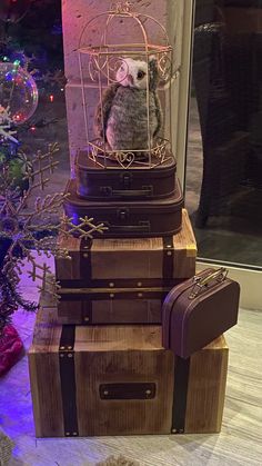 an owl sitting in a cage on top of suitcases next to a christmas tree