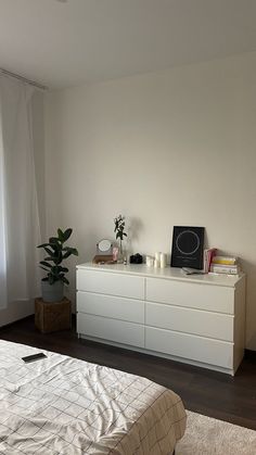 a bed sitting next to a white dresser in a bedroom under a window with curtains