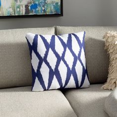 a blue and white pillow sitting on top of a gray couch next to a painting