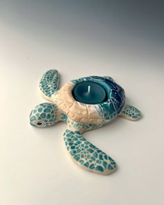 a teal turtle candle holder with a lit candle in it's shell on a white surface