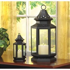 two black lanterns sitting on top of a table next to a potted plant