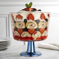 a trifle with strawberries, blueberries, and bananas in it on a gold pedestal