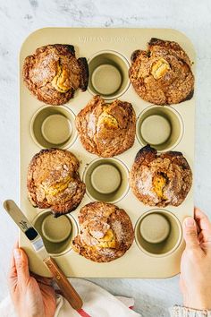 a muffin tray with several muffins in it and someone holding a knife