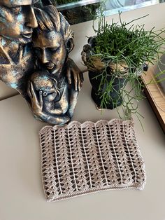 a small crocheted pot holder sits on a table next to a statue and some plants