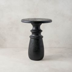 a small black table sitting on top of a white floor next to a gray wall