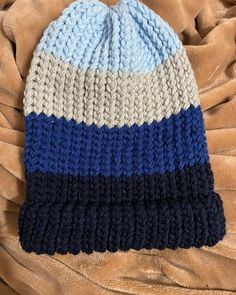 a blue, white and grey knitted hat laying on top of a brown blanket