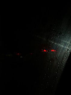 rain drops on the window at night with red lights in the dark room behind it