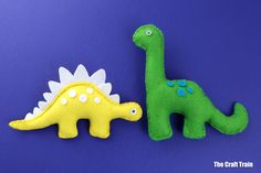 two felt dinosaurs sitting next to each other on a blue surface, one green and the other yellow