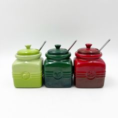 three different colored jars are lined up in a row on a white surface, one is green and the other is red