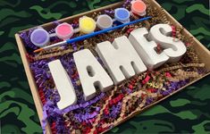 the word james spelled out in white letters on a camouflage background with paintbrushes and crayons