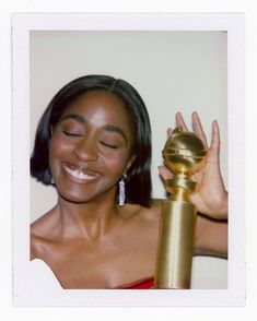 a woman holding up a golden object in her right hand and smiling at the camera