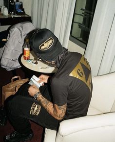 a man sitting in a chair holding a plate with food on it while wearing a hat