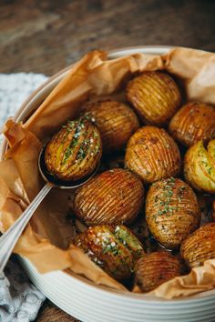 a bowl filled with cooked potatoes on top of a wooden table next to a fork