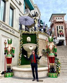 a man standing in front of a fountain with christmas decorations on it and two large nutcrackers behind him