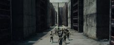 a group of people walking down a street next to tall concrete buildings in the dark