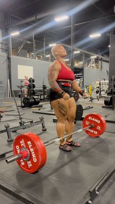 a woman in a red top is doing squats with barbells