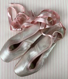 two ballet shoes with pink ribbon tied around them on a striped sheeted surface,