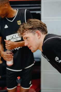 two men in black jerseys standing next to each other with one holding a water bottle