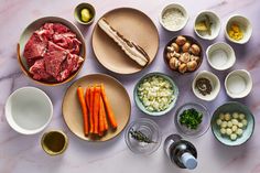 an assortment of meats and vegetables are arranged in bowls on a marble countertop