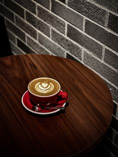 a cappuccino sitting on top of a wooden table next to a brick wall