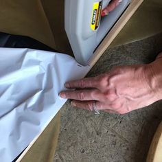 a person's hand on top of a piece of paper next to a white container