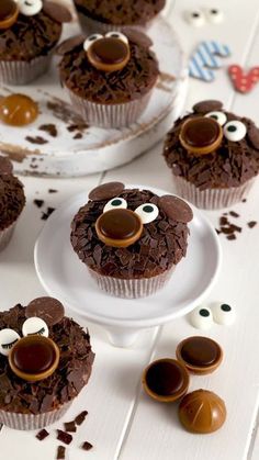 chocolate cupcakes with googly eyes and noses on white plates, surrounded by candy candies