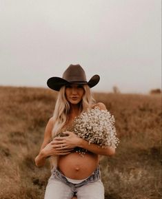 a pregnant woman wearing a cowboy hat and holding a bouquet of baby's breath