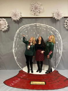 three women standing in front of a snow globe with their hands up to the side