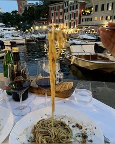 a plate of spaghetti being served at an outdoor table with boats in the water behind it