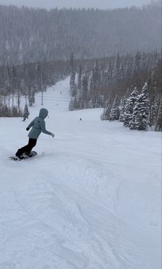 a person riding a snowboard down the side of a snow covered ski slope on a cloudy day