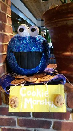 a cookie monster sitting on top of a sign next to a brick wall and potted plant