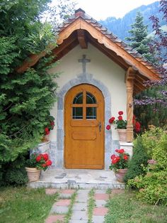 a small house with a wooden door surrounded by greenery and flowers in front of it