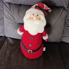 a red santa clause sitting on top of a couch next to a gray sofa pillow