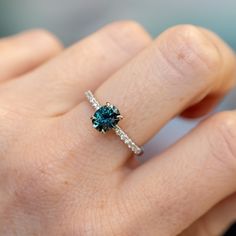 a woman's hand holding a ring with a blue diamond in it and diamonds around the band