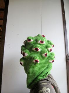 a person wearing a green knitted head covering with red eyes and fangs on it