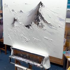 an artist's easel in front of a large painting with mountains on it