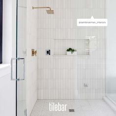 a white tiled bathroom with glass shower doors and shelves on the wall next to it