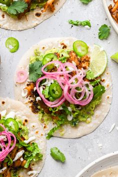 three tortillas with meat, onions and cilantro on a white surface