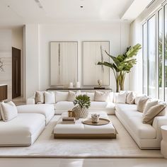 a living room filled with lots of white furniture next to tall glass windows on the wall