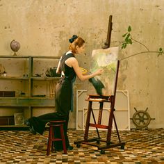 a woman is painting on an easel in a room with tile flooring and walls