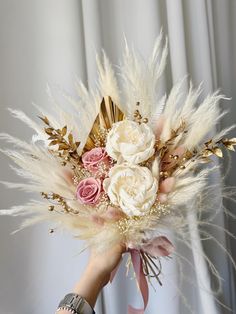 a woman holding a bouquet of flowers and feathers in front of a white curtained wall