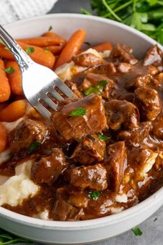 a bowl filled with meat and potatoes covered in gravy next to carrots