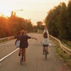 two people riding bikes on a road with trees in the background and one person raising their arms