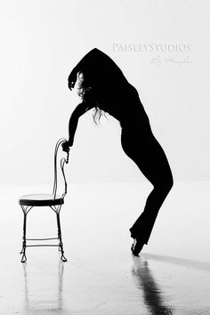 a black and white photo of a person bending over with a chair in front of them