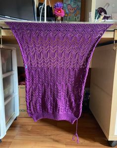 a purple knitted blanket hanging from a clothes line in front of a computer desk