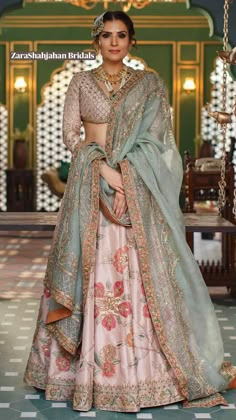 a woman in a pink and green lehenga is standing on a swing with chains hanging from the ceiling