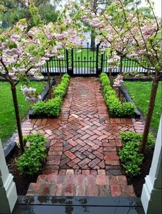 a brick pathway with trees and flowers in the background, leading to a gated area