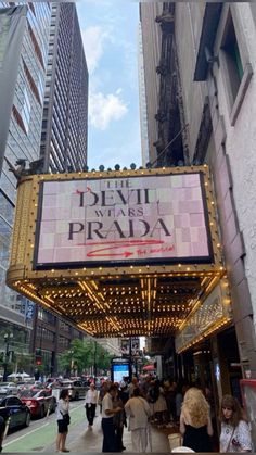 people walking down the sidewalk in front of a theater marquee with lights on it