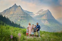 a family standing on top of a lush green hillside with mountains in the back ground