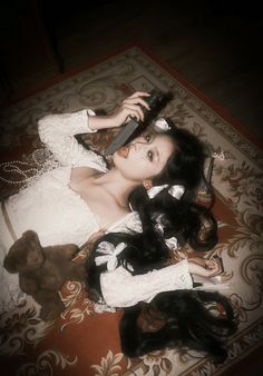 a woman laying on top of a rug next to a teddy bear wearing a dress